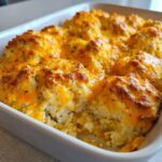 Close-up of baked chicken cobbler topped with melted cheddar cheese and herbs in a white dish.
