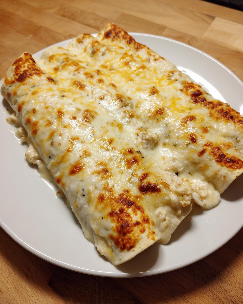 Close-up of three baked white chicken enchiladas smothered in melted, bubbly white cheese sauce.