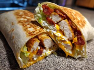 Close-up of a grilled chicken bacon ranch wrap cut in half, showing seasoned chicken, bacon, cheese, and ranch dressing.