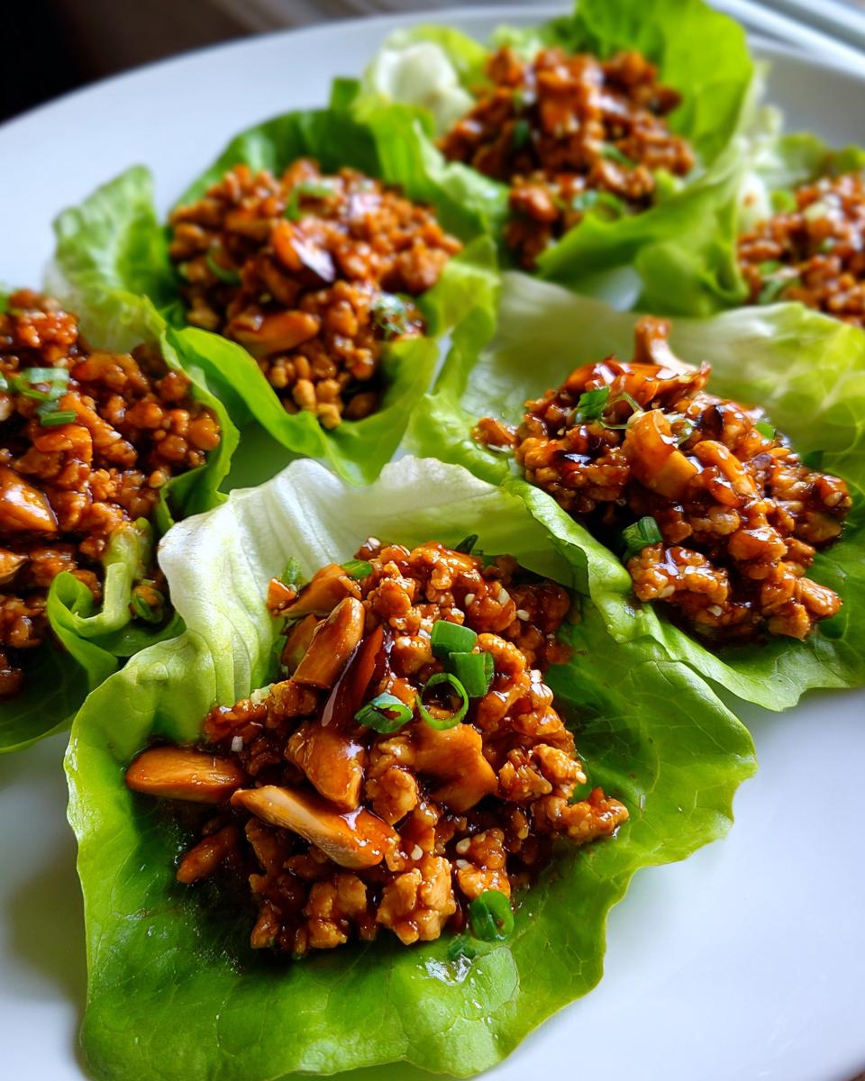 Close-up of several servings of saucy chicken lettuce wraps garnished with green onions on a white plate.