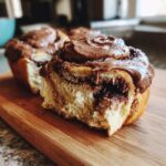 Close-up of a soft, fluffy chocolate cinnamon rolls slice showing the rich chocolate swirl and thick chocolate frosting.