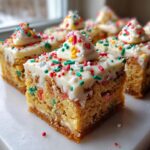 A close-up of square slices of Christmas tree cheesecake bars topped with white frosting and festive sprinkles.