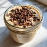 Close-up of cookie dough overnight oats in a glass jar, generously topped with mini chocolate chips.