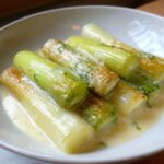 Several pieces of tender braised leeks swimming in a creamy white sauce, garnished with herbs.