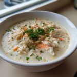 A close-up of a bowl of creamy crab soup loaded with shredded crab meat, garnished with fresh parsley and paprika.