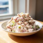 A generous mound of creamy ham salad recipe mixed with diced ham and green celery in a white bowl.