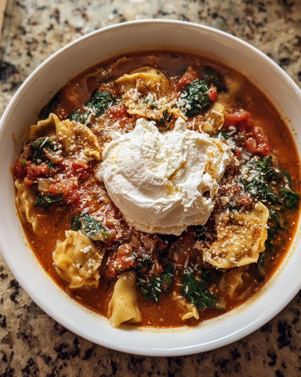 A close-up of a bowl of creamy lasagna soup featuring pasta, spinach, tomato broth, and a large dollop of ricotta cheese.