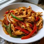 A white bowl filled with seasoned, shredded chicken mixed with vibrant red and green bell pepper strips for crockpot chicken fajitas.