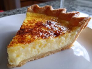 A close-up of a thick slice of creamy custard pie showing the rich filling and a beautifully caramelized, torched top.