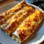 Three baked easy chicken enchiladas covered in melted, bubbly, golden-brown cheese on a white plate.