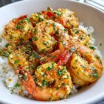 Close-up of succulent Hawaiian garlic shrimp coated in a rich, garlicky sauce and fresh parsley, served over white rice in a bowl.