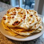 A stack of freshly cooked pita bread rounds with golden-brown and charred spots resting on a white plate.