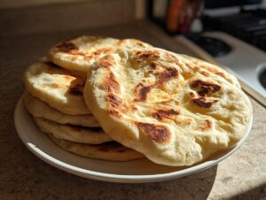 A stack of freshly cooked, slightly charred pita bread resting on a white plate in natural light.