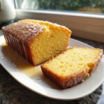 A moist lemon olive oil cake loaf, partially sliced, drizzled with a thick, sweet glaze.