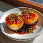 Two halves of beautifully rich, orange-yolked marinated eggs, drizzled with sauce and topped with sesame seeds and scallions.