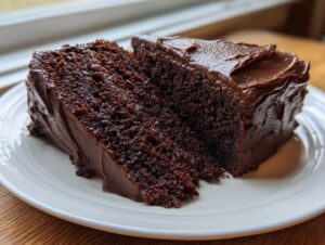 Two thick slices of incredibly moist chocolate cake covered in rich, dark chocolate frosting on a white plate.