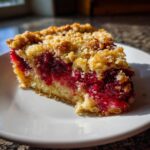 Close-up of a rich slice of Nantucket cranberry pie showing bright red filling and golden crumb topping.