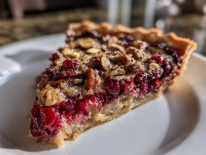 Close-up of a slice of rich Nantucket cranberry pie featuring bright red cranberries and a pecan topping on a white plate.