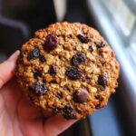 A hand holding a freshly baked, hearty oatmeal raisin breakfast cookie packed with oats and dried fruit.