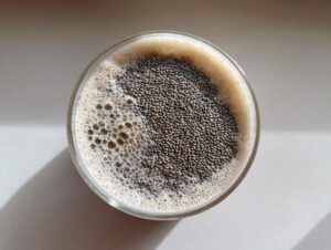 Overhead view of a glass containing high-protein chia seed pudding topped with a layer of dark chia seeds and light foam.