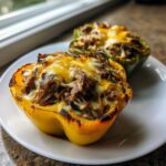 Close-up of a baked yellow bell pepper half stuffed with savory meat and topped with melted cheese, part of the philly cheesesteak stuffed peppers recipe.