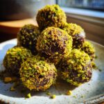 A close-up stack of rich, dark dubai chocolate balls generously coated in bright green crushed pistachios.