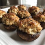 A close-up of several baked sausage stuffed mushrooms with golden, crispy tops, served on a white platter.