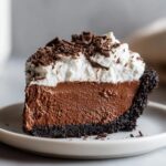 A decadent slice of chocolate mousse pie featuring a dark crust, thick chocolate filling, and topped with whipped cream and chocolate shavings.