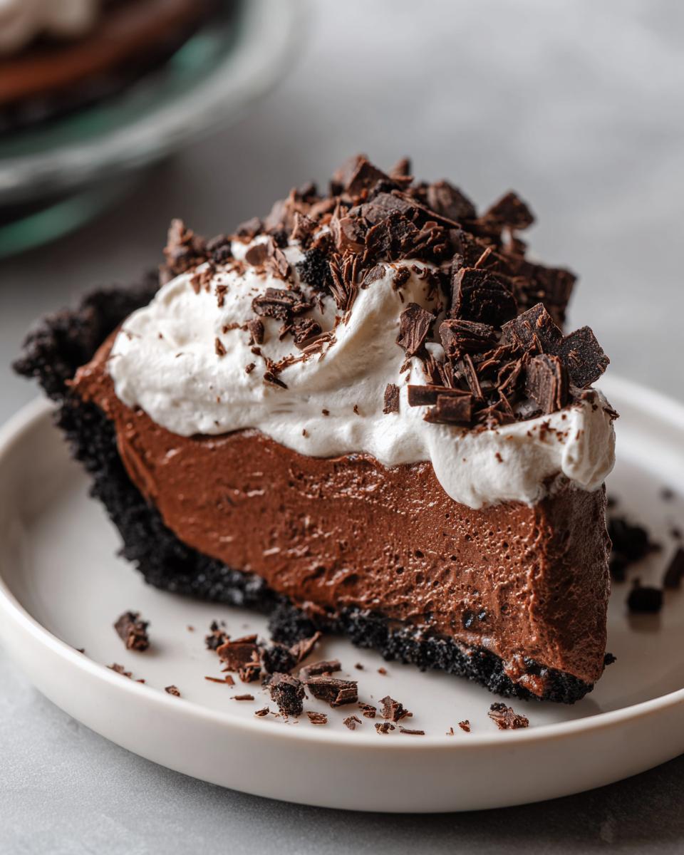 A decadent slice of chocolate mousse pie featuring a dark crust, rich chocolate filling, whipped cream, and chocolate shavings.