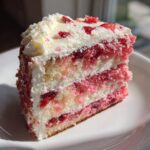 A close-up, sunlit slice of layered strawberry cake featuring pink sponge, white cream filling, and strawberry pieces.