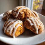 A stack of soft, orange persimmon cookies drizzled with white icing, resting on a white plate.