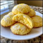 A stack of soft ricotta cookies topped with lemon glaze and zest, one cookie broken open showing the interior texture.