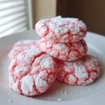 A stack of vibrant pink, crinkle-cut strawberry cake mix cookies dusted heavily with powdered sugar on a white plate.