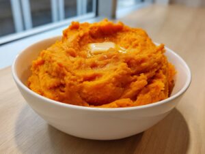 A white bowl filled with bright orange, fluffy mashed sweet potatoes topped with a melting pat of butter.