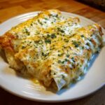 Close-up of three delicious white chicken enchiladas covered in melted white and yellow cheese and sprinkled with parsley.