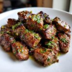 Close-up of perfectly seared steak bites glistening with garlic butter and fresh parsley.