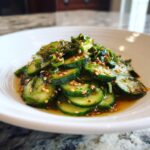 Close-up of sliced cucumbers tossed in a savory dressing with sesame seeds, part of an amazing asian cucumber salad.
