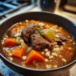 Close-up of a rich bowl of beef barley soup with chunks of beef, carrots, celery, and barley.