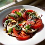 Close-up of a beautiful caprese salad featuring alternating slices of red tomato and fresh mozzarella, drizzled with balsamic glaze and basil.