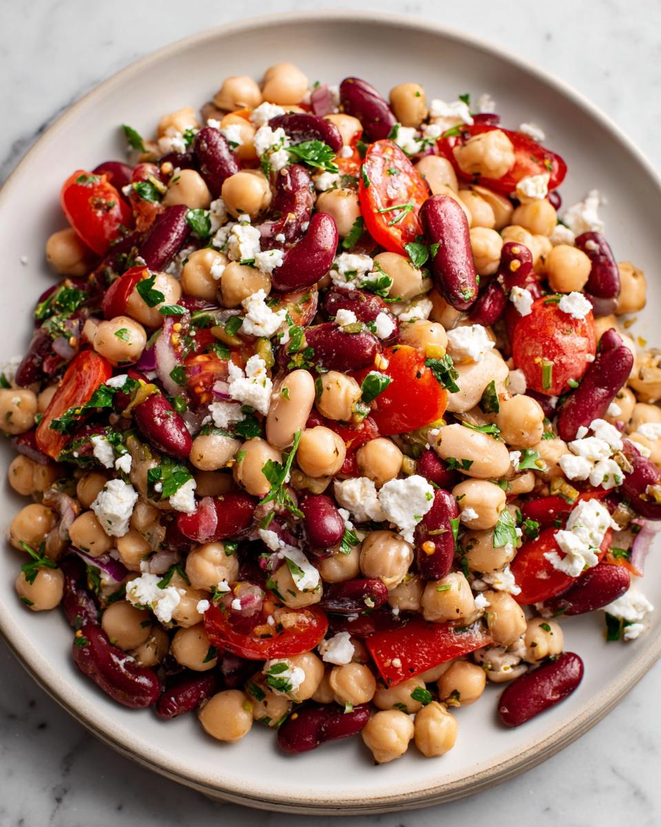 Close-up of a vibrant bowl of high protein bean salad featuring chickpeas, kidney beans, tomatoes, and feta.