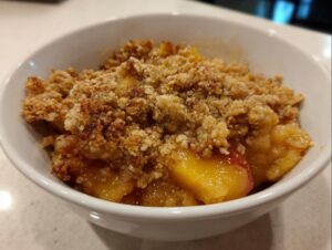 Close-up of a warm serving of amazing peach crisp with a thick, crunchy topping in a white bowl.