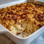 Close-up of creamy popper dip in a white baking dish, topped with golden breadcrumbs and bacon.