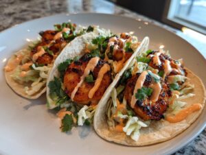 Three delicious shrimp taco shells filled with blackened shrimp, shredded cabbage, and drizzled with spicy orange sauce.