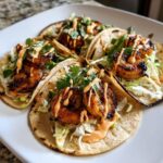 Four delicious shrimp taco servings piled high with blackened shrimp, slaw, cilantro, and drizzled with spicy sauce.