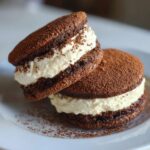 Two decadent tiramisu cookies stacked on a white plate, featuring dark chocolate cakes and creamy mascarpone filling dusted with cocoa.
