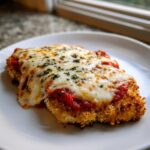 A close-up of a perfectly baked chicken parmesan cutlet topped with rich tomato sauce and melted mozzarella cheese.