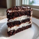 A tall slice of brownie refrigerator cake showing three dark chocolate layers separated by thick white cream filling.