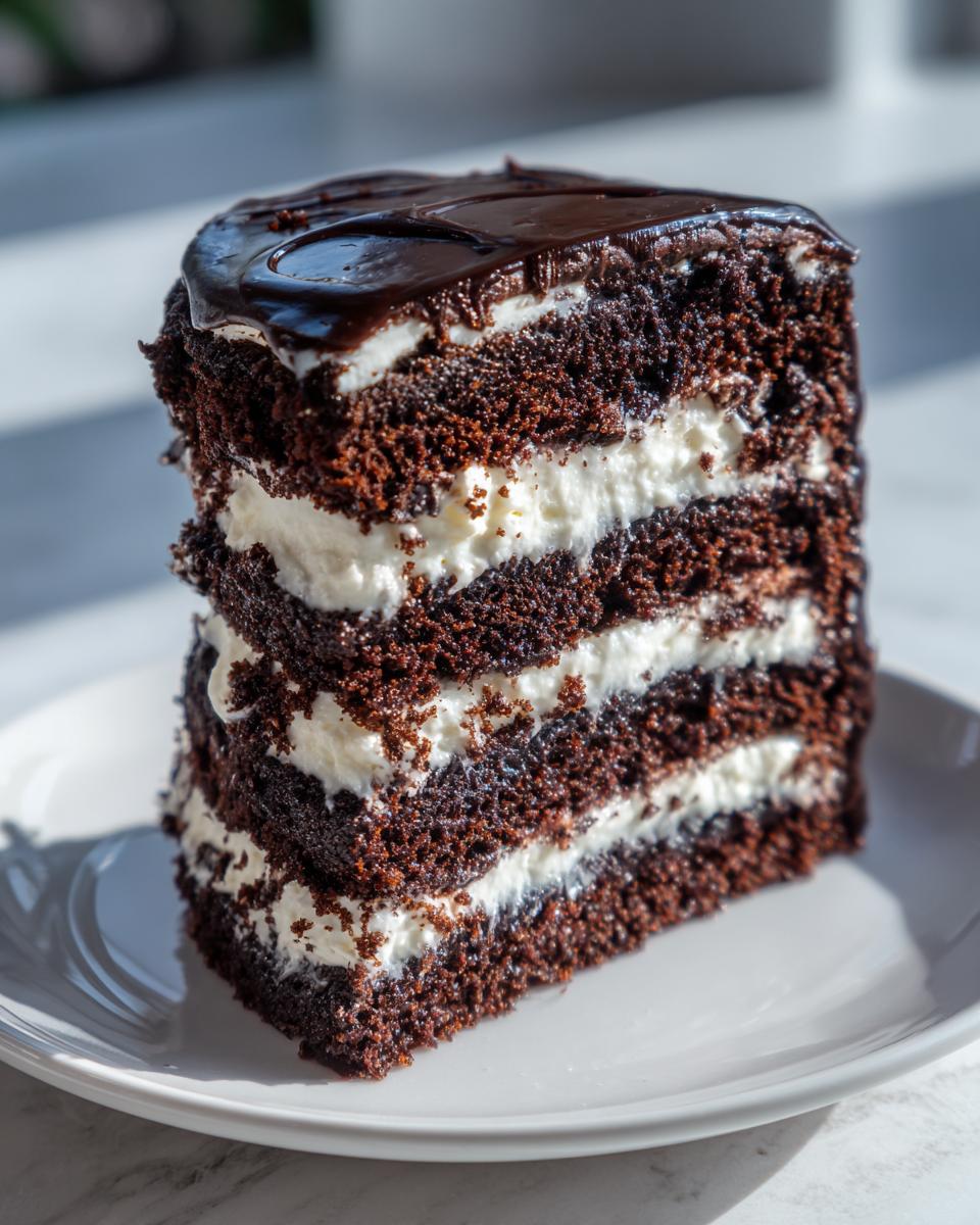 A tall, layered slice of brownie refrigerator cake with dark chocolate cake and white cream filling, topped with chocolate ganache.