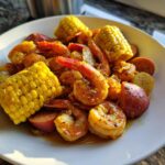 Close-up of a serving of Cajun shrimp boil featuring seasoned shrimp, corn on the cob, potatoes, and sausage slices.