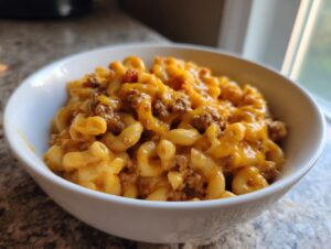 A close-up of a white bowl filled with creamy, cheesy taco pasta mixed with seasoned ground beef.